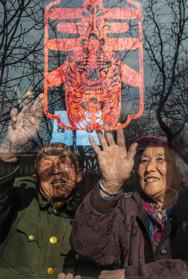 臘月里，霍州市師莊鄉(xiāng)馮南垣村村民師榮光(左)在災(zāi)后重建的新家里貼窗花。(霍州市委宣傳部供圖)