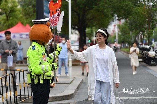 6月7日上午9時(shí)，隨著鈴聲的響起，2023年江西高考正式開考，江西省的53.57萬考生以縣（區(qū)）為單位隨機(jī)安排在全省256個(gè)考點(diǎn)、18968個(gè)考場(chǎng)參加高考。圖為“小熊交警”和考生擊掌鼓勵(lì)。 人民網(wǎng)記者 時(shí)雨攝