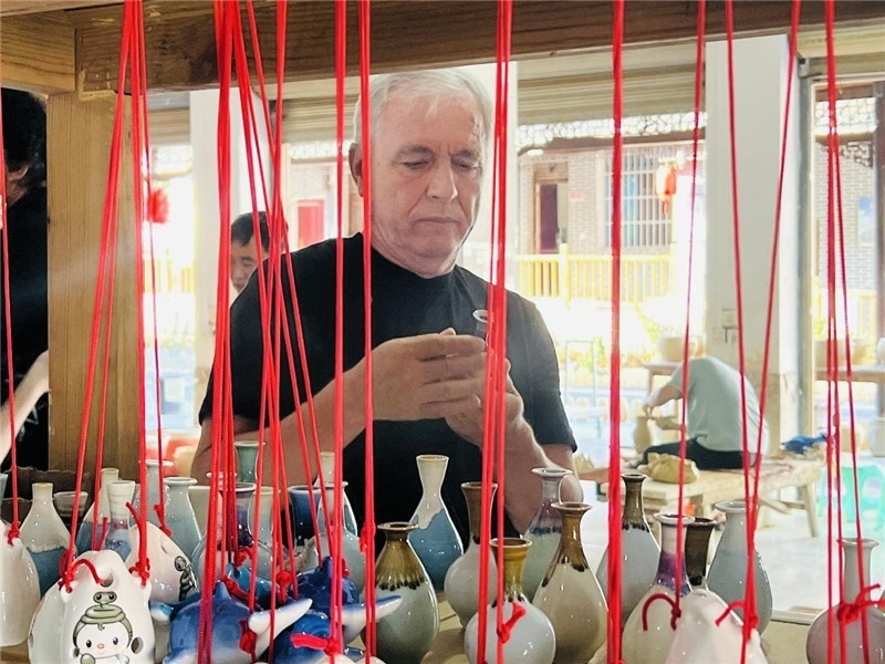 鄉(xiāng)愁如同一根根紅線，將游子與故鄉(xiāng)永遠地牽連到一起。花茂村陶藝文化創(chuàng)意一條街的母氏陶藝館內(nèi)，紅線吊著陶瓶，思緒游走萬里。摩爾多瓦“信息標簽”通訊社社長亞歷山大·塔納斯端詳著館內(nèi)展示的陶藝作品，并挑選出心儀的小擺件帶回摩爾多瓦，也帶走花茂村的“鄉(xiāng)愁”。（張亞欣攝）