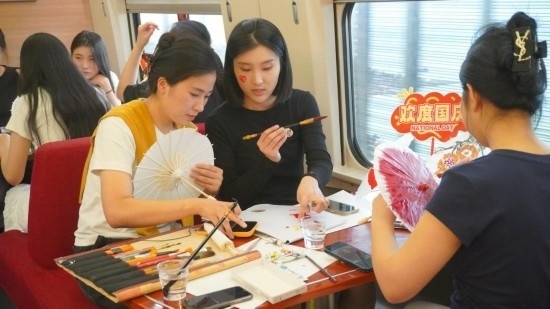 10月1日，旅客們?cè)贕1634次列車上給油紙傘作畫。新華社記者周義 攝